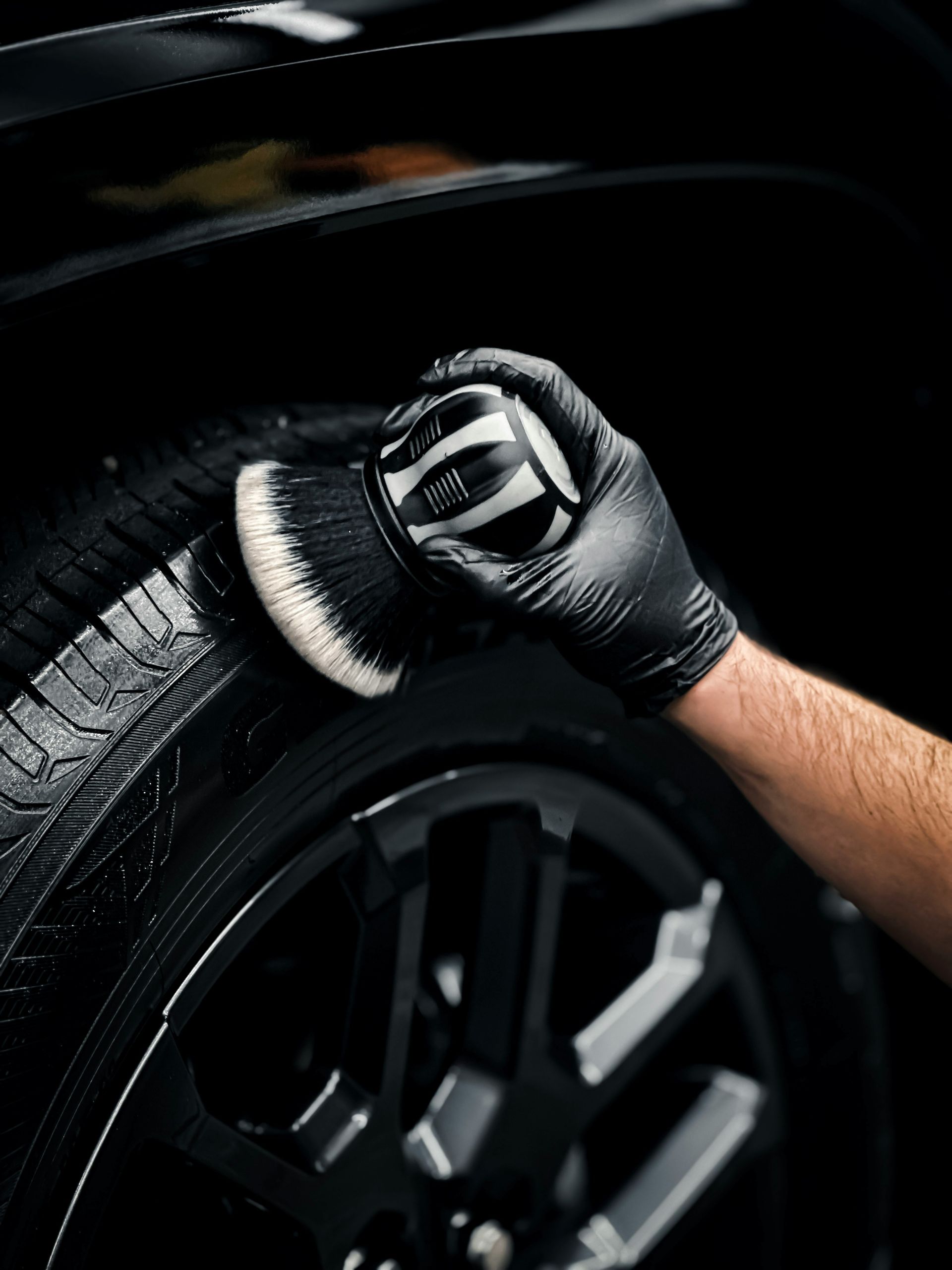 A person in a black glove cleaning a car tire with a brush